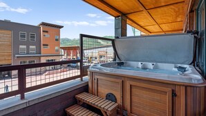 A wooden deck with a hot tub, wooden benches, and a view of buildings and mountains. - Newpark 217 | Private Hot Tub | Kitchenette | Fireplace | Washer & Dryer | Balcony | Pool & Hot Tub (Park City)