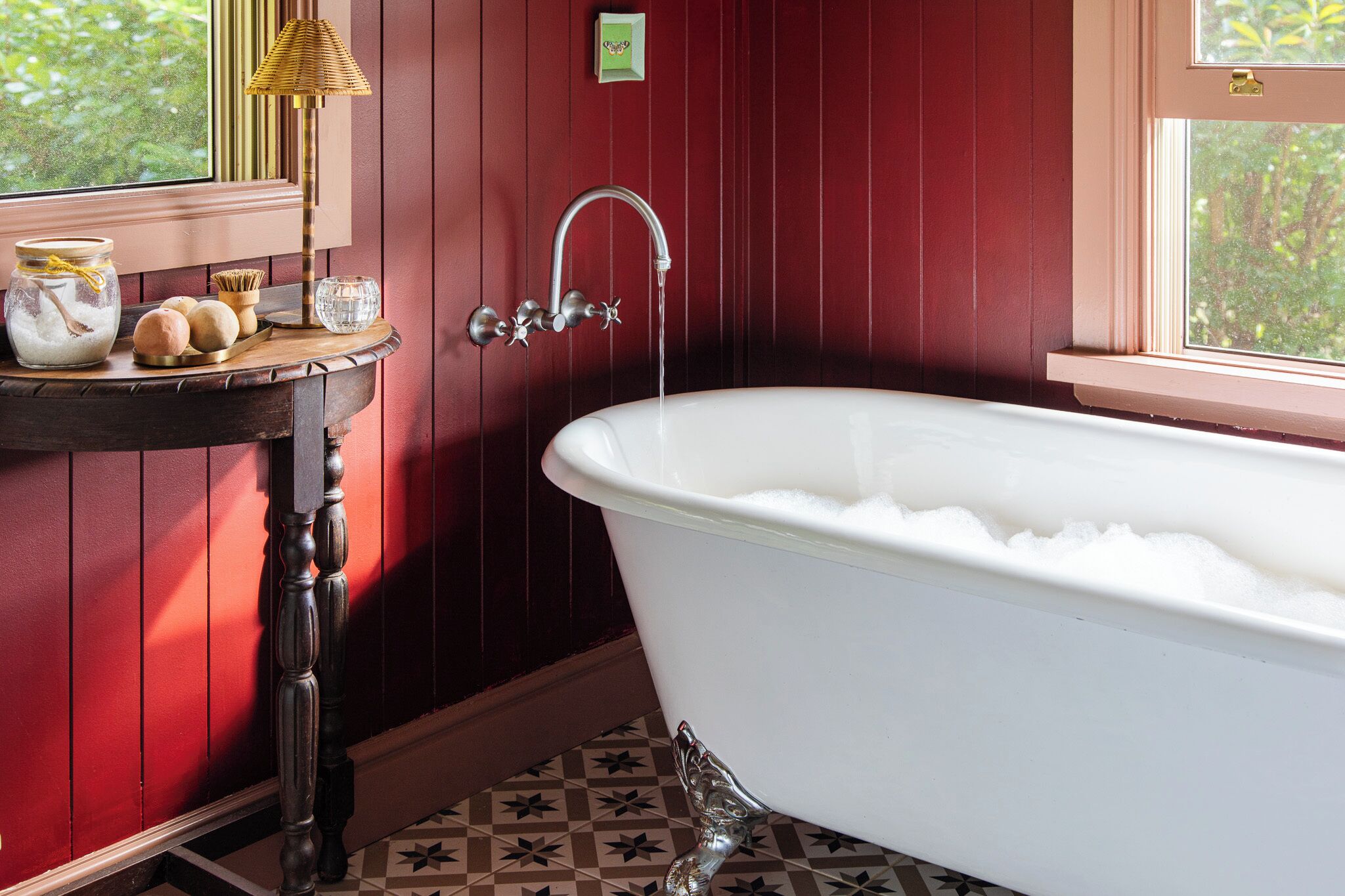 Ein Badezimmer mit einer weißen Badewanne, einem Holzkosmetikschrank, einem Messingarmaturen und einem Fenster mit Blick auf Grünflächen.