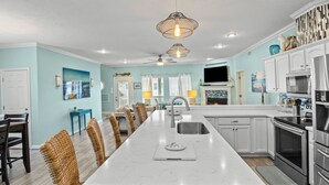 Una cocina moderna con una isla central, armarios blancos, electrodomésticos de acero inoxidable y sillas de mimbre.
