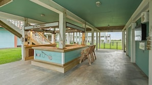 Un espacio al aire libre cubierto con barra de madera y asientos, una escalera y vista a un campo verde.