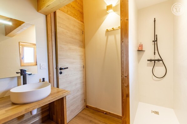 A bathroom with a wooden vanity, a white sink, a mirror, and a shower with a handheld showerhead.