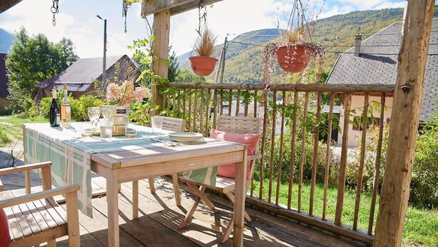 Een terras van hout buiten, met een eettafel, omringd door stoelen en een hangplanter.