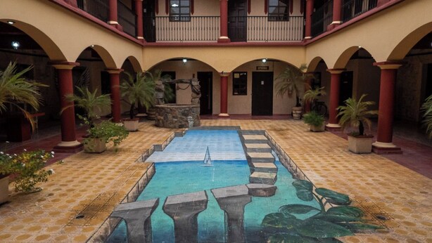 Une cour intérieure avec une piscine centrale, entourée d’arcades et de plantes en pot.
