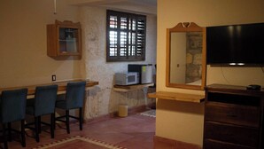 Un coin repas avec une table en bois, des chaises bleues, un four à micro-ondes et un téléviseur posé sur un meuble en bois.