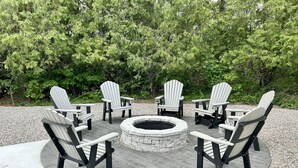 A circular fire pit surrounded by Adirondack chairs on a wooden deck.