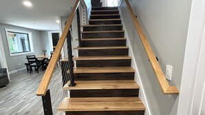 A staircase with wooden steps and metal railings, leading to a second-floor area with a dining table and chairs.