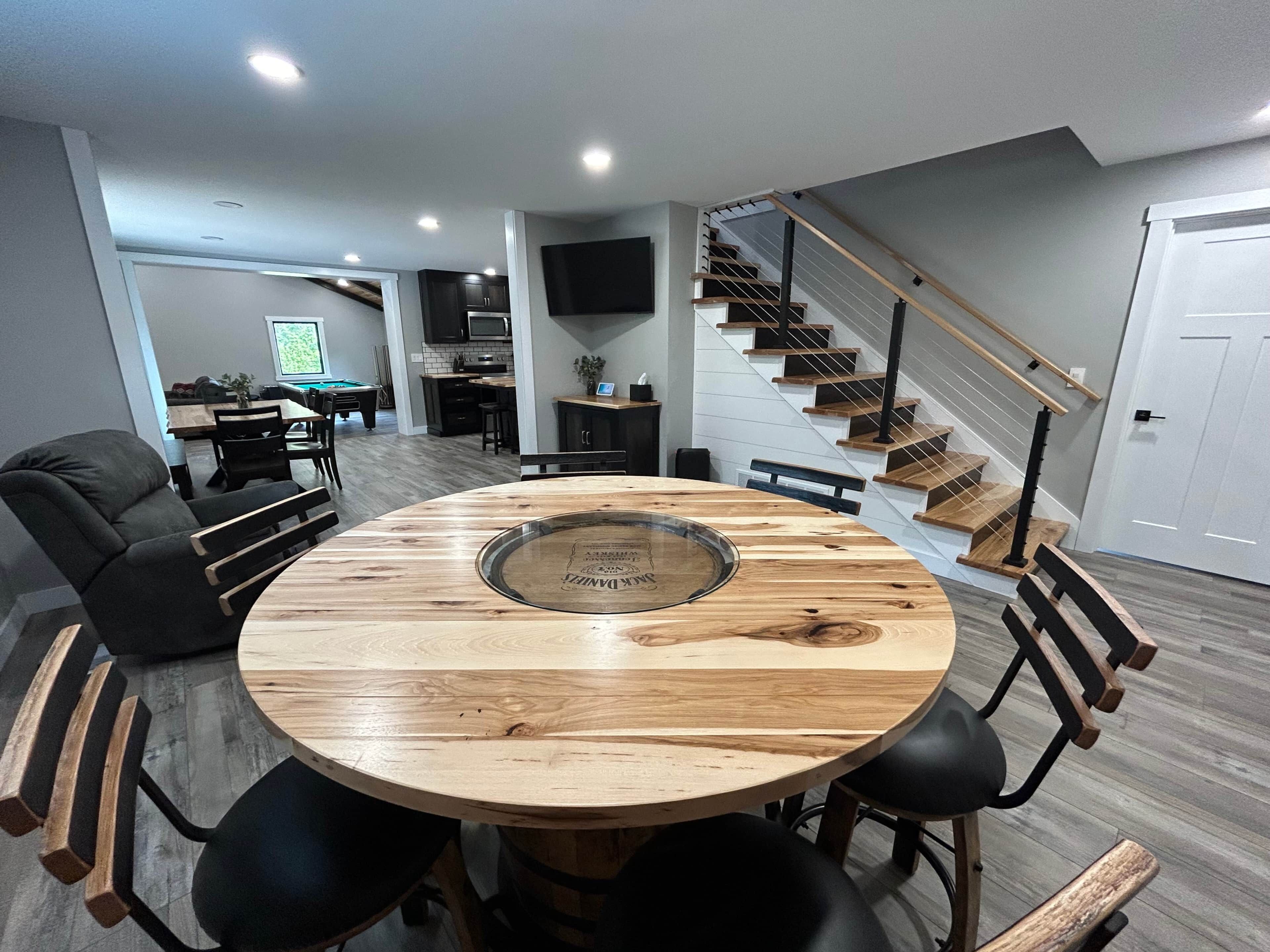 Un espace repas moderne avec une table ronde en bois et des chaises noires, un escalier avec des marches en bois, et une cuisine en arrière-plan.