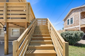 Una scala in legno conduce a un edificio con facciata bianca e un piccolo giardino.