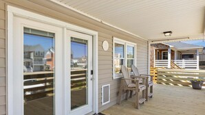 A covered porch with a wooden deck, a set of Adirondack chairs, and a small table. - Sandy Keys 1 *Pet Friendly*2min walk to beach! (Kill Devil Hills)