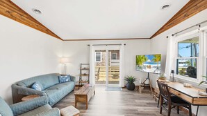 A spacious living area with a sofa, coffee table, and a dining table with chairs. There is a sliding glass door leading to an outdoor deck. - Sandy Keys 1 *Pet Friendly*2min walk to beach! (Kill Devil Hills)