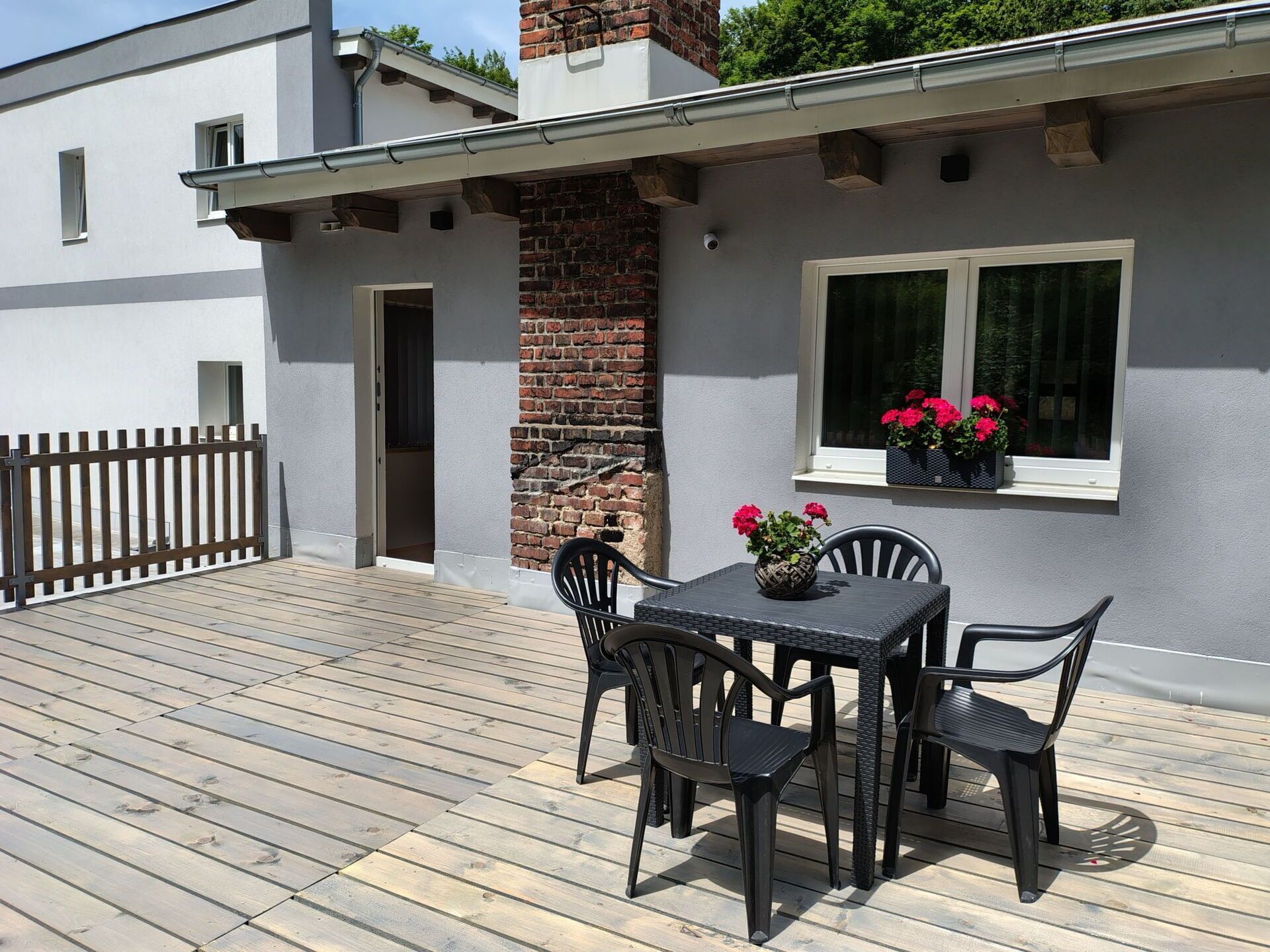 Une terrasse avec une table et des chaises, un mur en briques et une fenêtre ornée de fleurs.