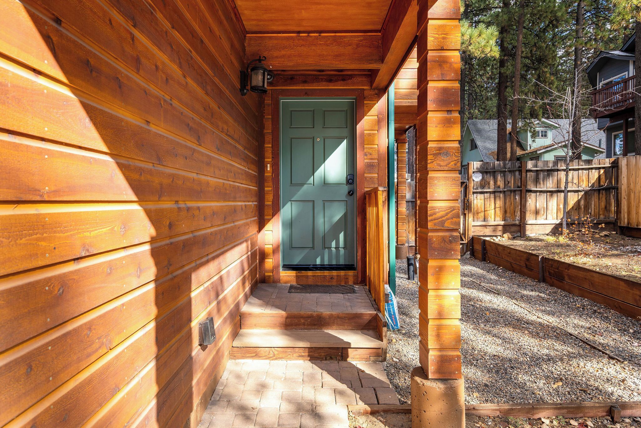Una cabaña de madera con puerta verde, un porche de madera y un sendero de grava que lleva a la puerta.