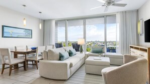 A modern hotel room with a large window, a ceiling fan, a dining area with a table and chairs, and a flat-screen TV. - Marriott's Crystal Shores - 2 bedroom luxury villa on Crescent Beach in Marco (Marco Island)