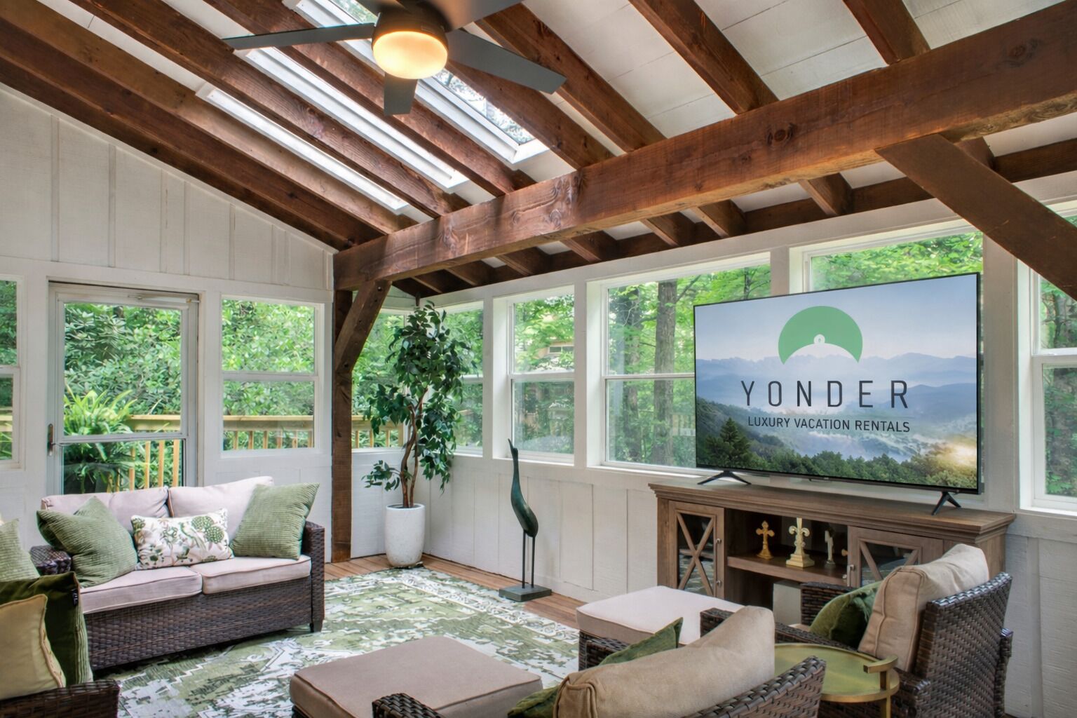 Ein gemütliches Wohnzimmer mit einem großen Fernseher, Holzbalken und Blick auf Grünflächen.