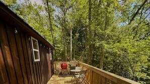 A wooden deck with a covered seating area, a grill, and a small table. - Adventurer’s Nook | Tiny Home w/ Hot Tub & Firepit (Campton)