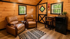 Ein Interieur einer Holzhütte mit zwei Ledersesseln, einem kleinen Tisch, einem Kühlschrank und einem Feuerlöscher.