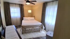 A hotel room with a bed, a desk, a ceiling fan, and a trash can.