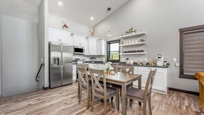 Una cocina moderna con armarios blancos, un refrigerador de acero inoxidable y un comedor con sillas y una mesa de madera.