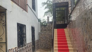 A staircase with a red carpet leading to a gated entrance, surrounded by a stone wall and a white building with a balcony. - Appartment and studios in kribi. (Kribi)