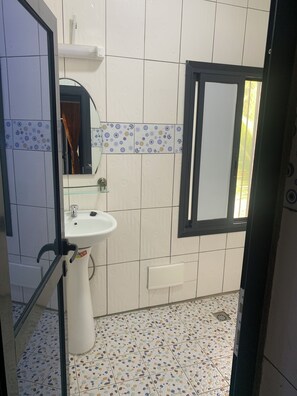 A bathroom with a white sink, a mirror, and a tiled floor. - Appartment and studios in kribi. (Kribi)