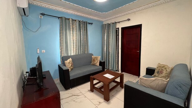 A living room with a sofa, a coffee table, a TV, and a red cabinet. - Appartment and studios in kribi. (Kribi)