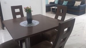 A dining area with a wooden table, six chairs, and a vase with flowers. There is a blue sofa with cushions in the background. - Appartment and studios in kribi. (Kribi)