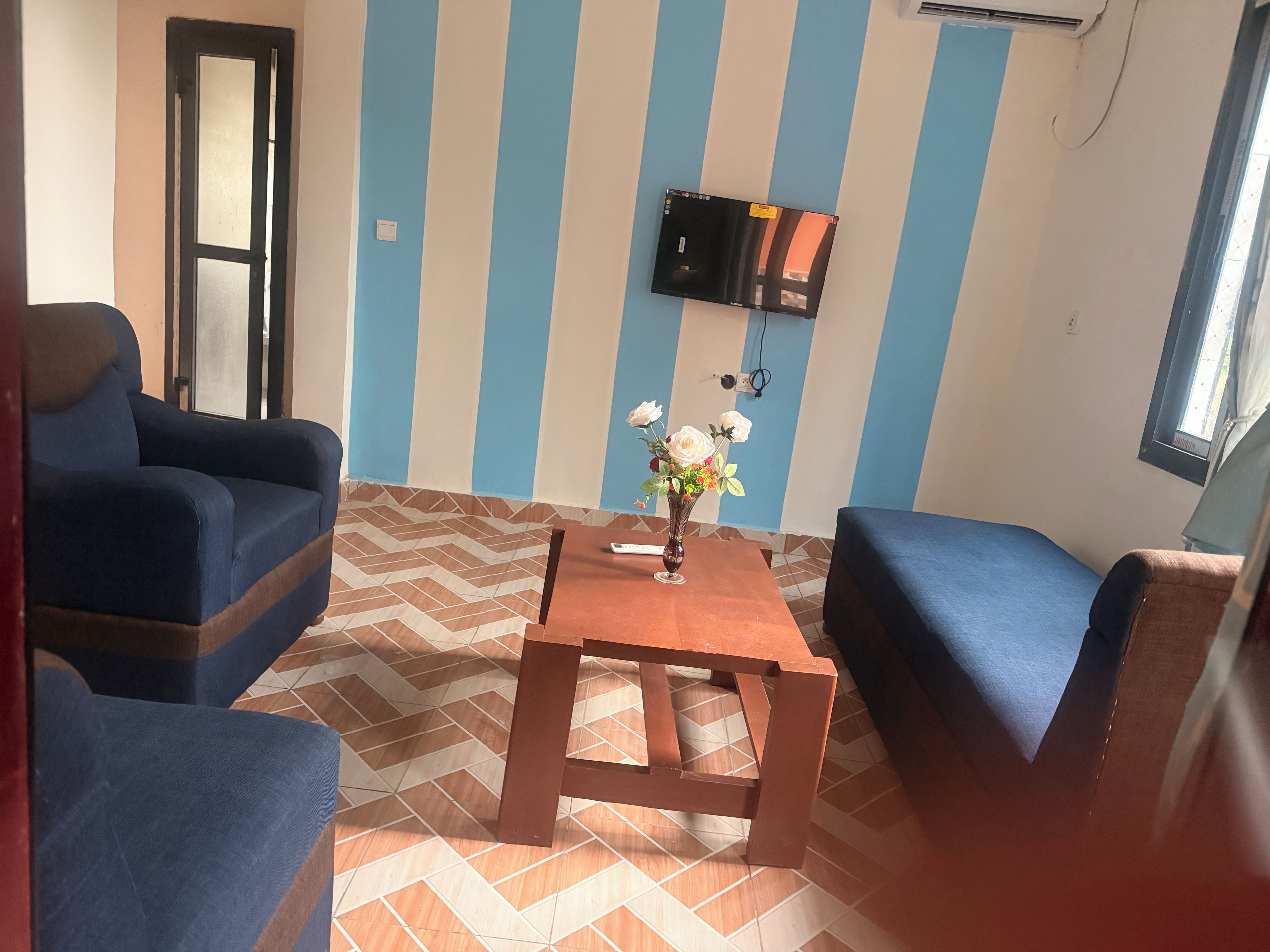 A room with striped walls, a flat-screen TV mounted on the wall, a wooden table, and blue upholstered chairs.