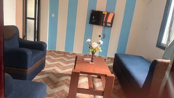 A room with striped walls, a flat-screen TV mounted on the wall, a wooden table, and blue upholstered chairs.