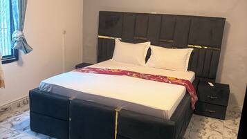 A bedroom with a bed, a nightstand, an air conditioning unit, and patterned floor tiles.