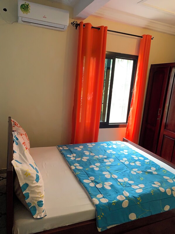 Un dormitorio con una cama, una ventana con cortinas naranjas y un equipo de aire acondicionado en la pared.