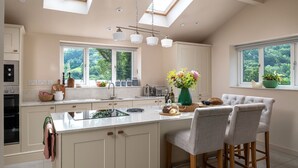 A modern kitchen with a central island, large windows, and a skylight. - Swn y Nant - Luxury Cottages (Wrexham)