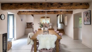 A spacious dining area with a wooden table and chairs, a rustic ceiling beam, and a view of the garden through a glass door. - Swn y Nant - Luxury Cottages (Wrexham)