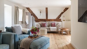 A living room with a blue sofa, a wooden coffee table with a vase of flowers, and a wooden floor. - Swn y Nant - Luxury Cottages (Wrexham)