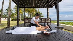 Une séance de massage en plein air, sur une terrasse en bois, avec vue sur l’océan et les palmiers.