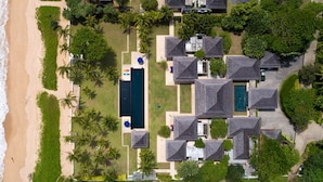 Vue aérienne d’un complexe hôtelier doté d’une plage, de plusieurs villas, d’une piscine et d’un aménagement paysager luxuriant.