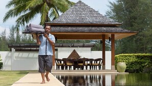 Un homme porte des serviettes enroulées, un gazebo, il y a une piscine et un coin repas avec des chaises et une table.