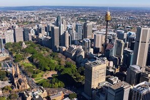 An aerial view of a cityscape with modern high-rise buildings, a prominent tower, and a green park area. - KozyGuru | Haymarket | Buzzy City Abode (Haymarket)