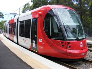 A modern tram with a red and white color scheme, number 2116, at a station platform. - KozyGuru | Haymarket | Buzzy City Abode (Haymarket)