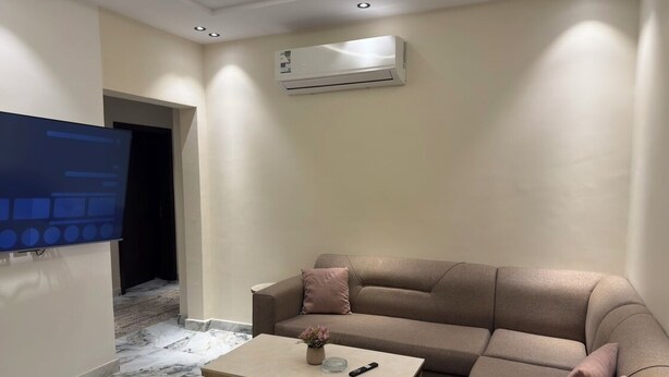 Un salon avec un canapé beige, une table basse, un téléviseur et un climatiseur.