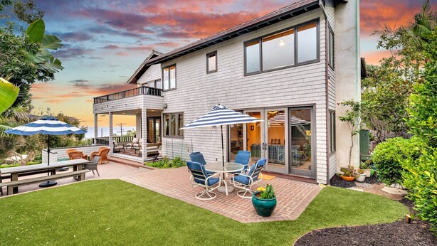 Una casa moderna de dos pisos con un patio, mobiliario exterior y un césped bien cuidado.