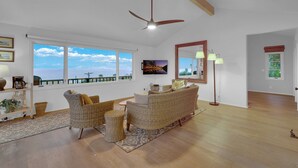Amplia sala de estar con gran ventanal, muebles de mimbre, ventilador de techo y vista al océano.