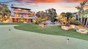 Una casa moderna de dos plantas con un césped cuidado y un campo de golf al frente.