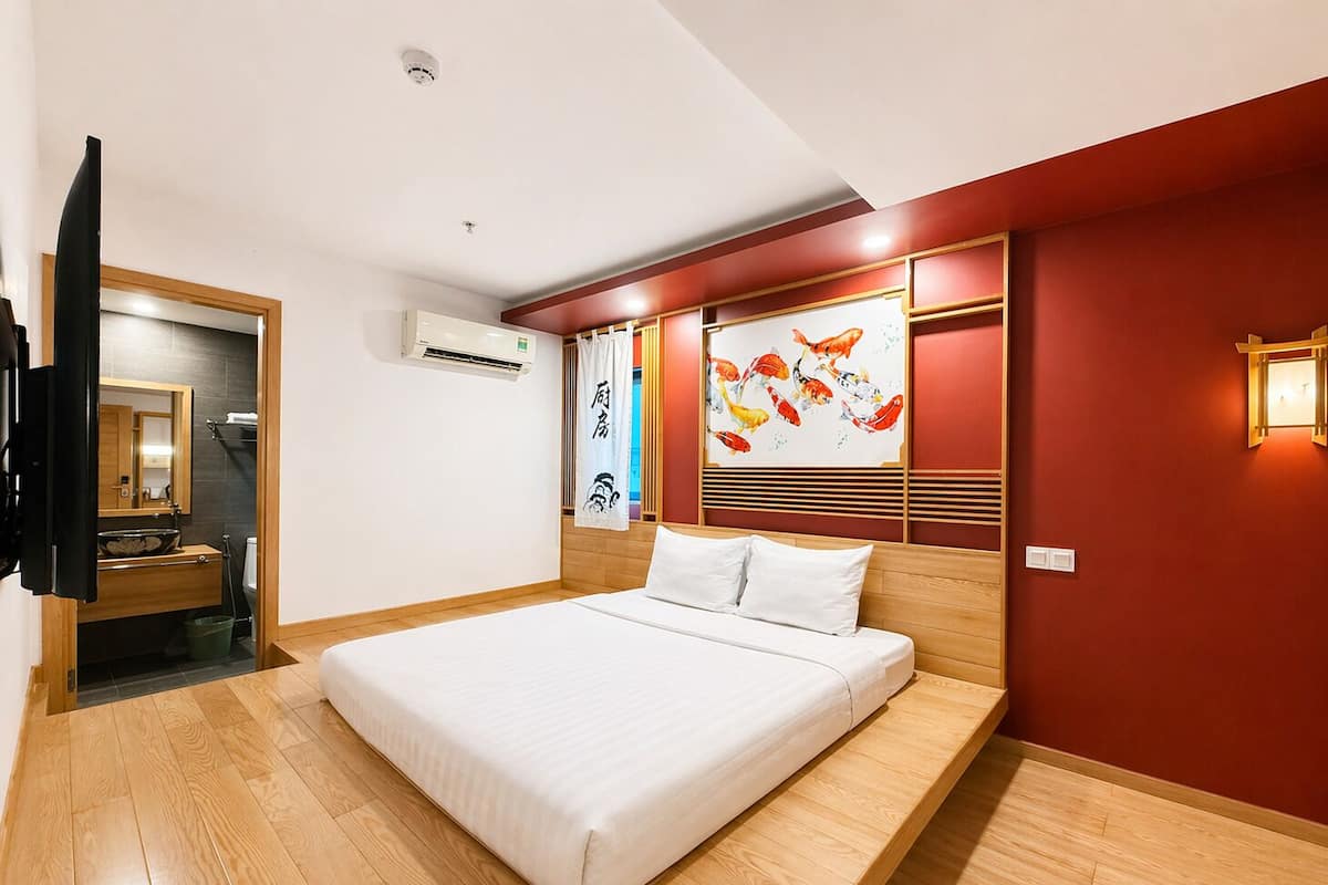 Una habitación de hotel moderna con una cama grande, suelo de madera, baño con espejo y lavamanos, y aire acondicionado de pared.