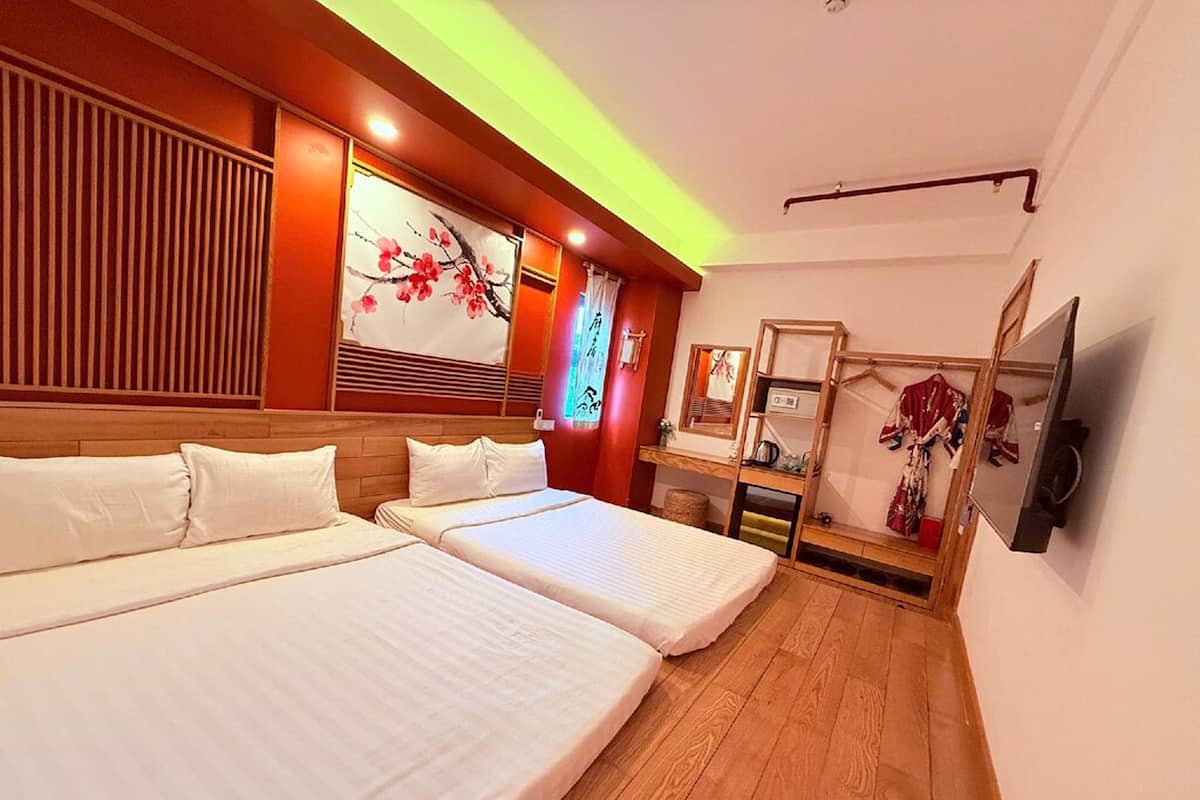 Habitación de hotel con dos camas, piso de madera, televisor montado en la pared y una ventana con diseño floral.