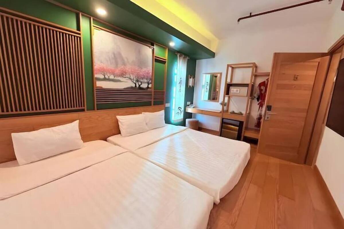 A hotel room with a large bed, a wooden headboard, a painting of cherry blossoms, a small desk with a mirror, and a wooden wardrobe.