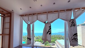 Una habitación con un ventanal grande, vigas de madera y vistas a un paisaje tropical.