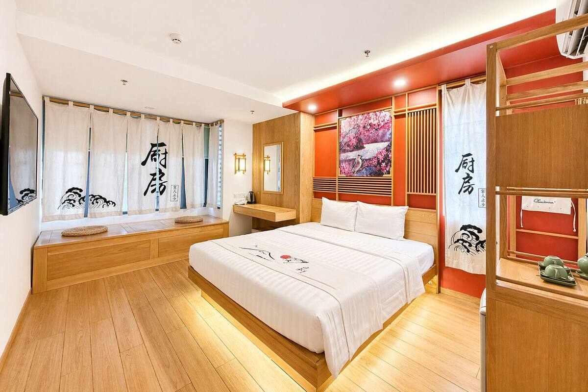 Habitación de hotel con cama, suelo de madera, ventana con cortinas, mesita de noche y un cuadro en la pared.