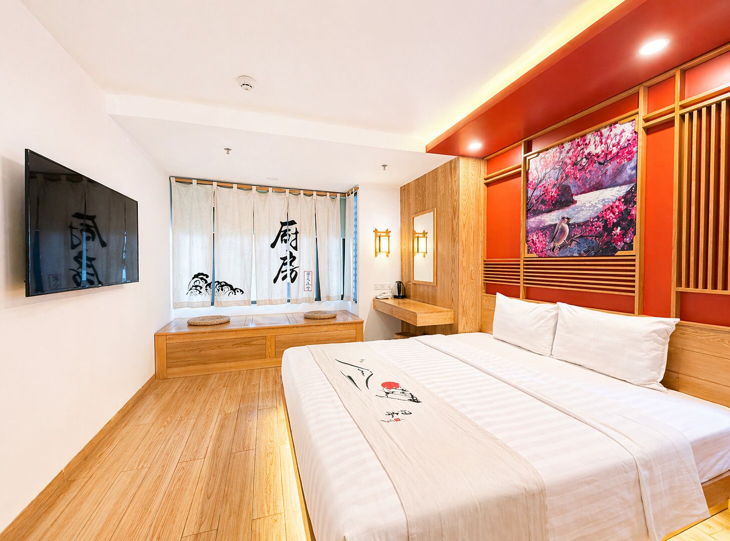 A hotel room with a bed, a wooden bench, a wall-mounted TV, a painting, and a Japanese-style curtain.