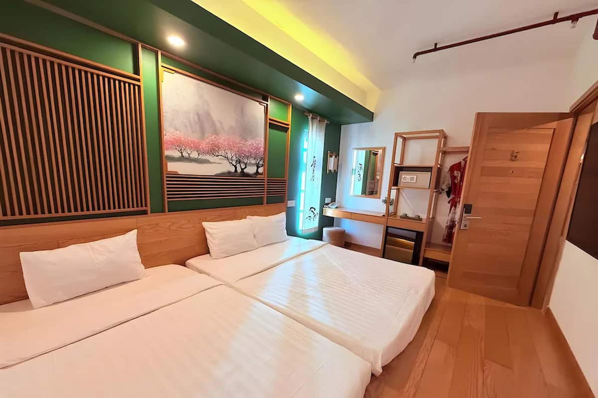 Habitación de hotel con dos camas, un escritorio, un espejo y una puerta.