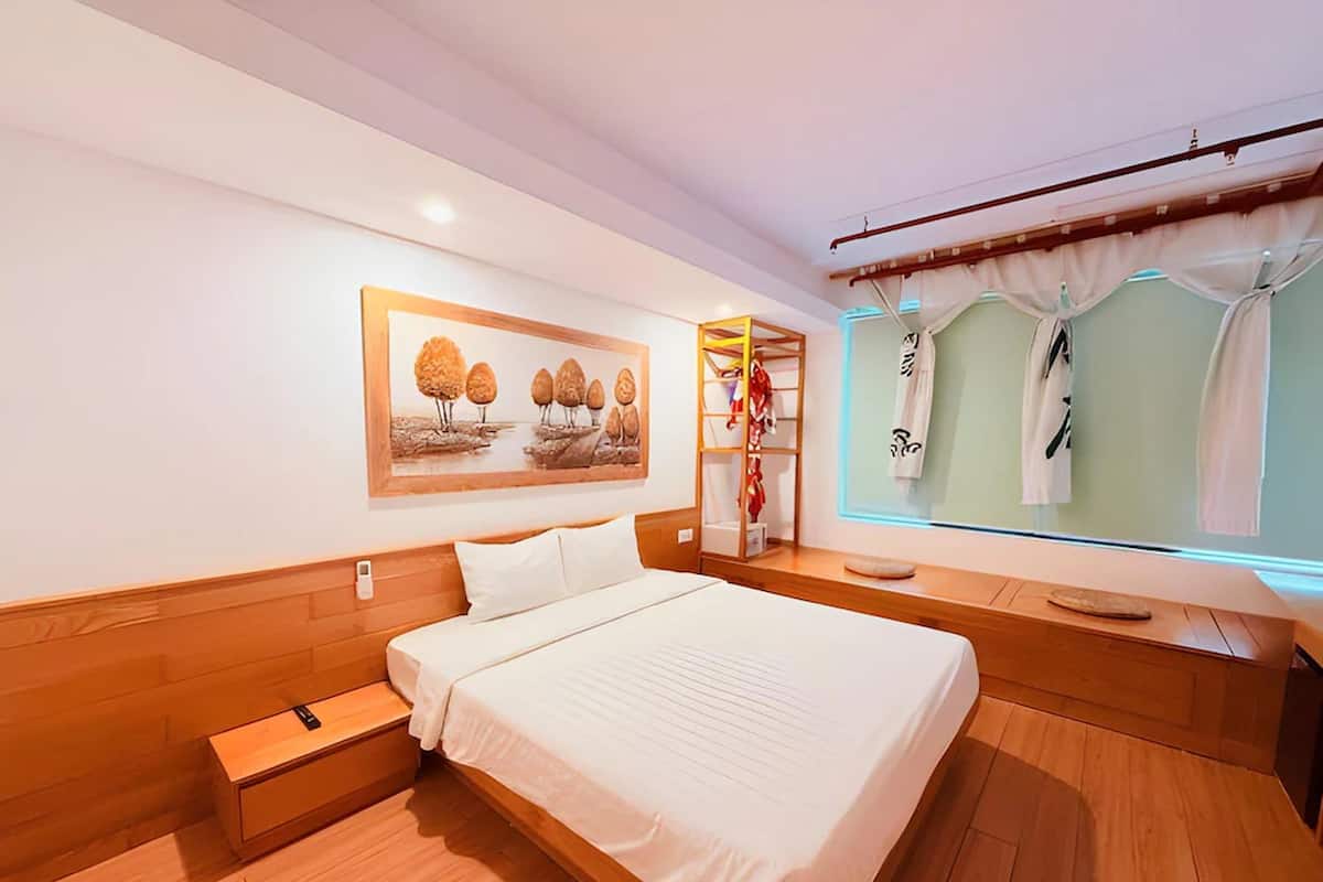 Una habitación de hotel con una cama de madera, una mesita de noche, un estante en la pared, un cuadro, un armario y una ventana con cortinas.